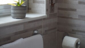 A bathroom with a window, a potted plant, a towel, and a toilet paper holder. - Al Teatro Greco (Syracuse)