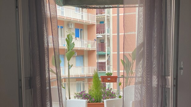 A hotel room with a bed, a balcony, and a view of a building with balconies. - Al Teatro Greco (Syracuse)