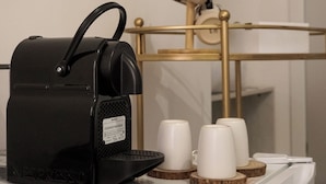 A black Nespresso coffee machine on a white tray with three white cups and a small clock on a gold stand in the background. - Al Teatro Greco (Syracuse)