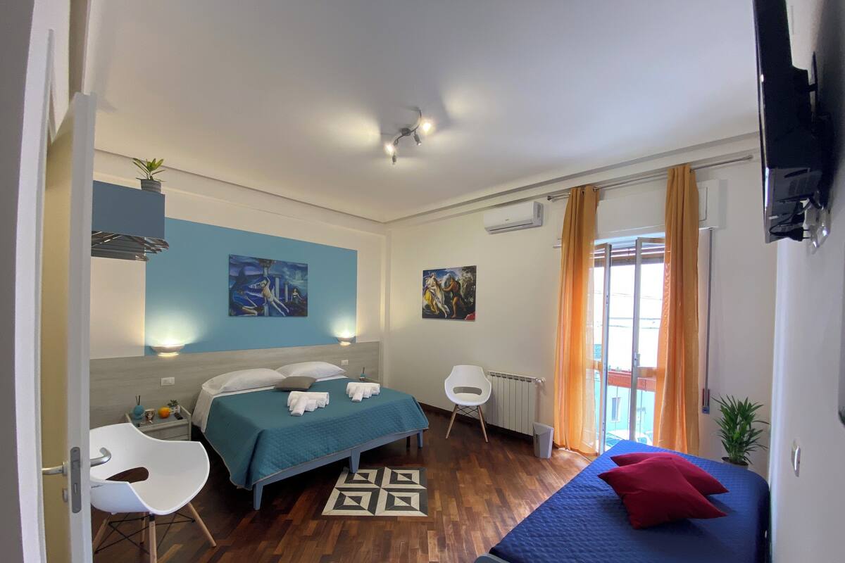 A bedroom with a bed, a sofa, a chair, a small table, and a painting on the wall.