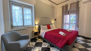 A hotel room with a bed, a chair, a nightstand, a window, and a view of the outside. - Al Teatro Greco (Syracuse)