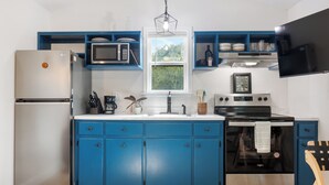A modern kitchen with blue cabinets, a stainless steel refrigerator, a microwave, a stove, and a window with a view of greenery. - Welcome to Casa Antigua – Your Perfect Getaway in San Marcos (San Marcos)