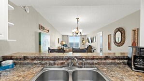 A kitchen with a double sink, granite countertop, and a view to the living area.