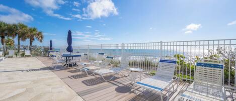 A sunlit outdoor seating area with lounge chairs and umbrellas, overlooking a body of water.