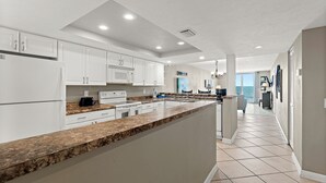 A modern kitchen with white cabinets, granite countertops, and a view to the living area.