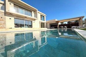 Ett modernt hus med en swimmingpool, stora fönster och en täckt uteplats.