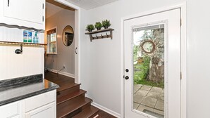 A clean, modern kitchen with white cabinets, a black countertop, and a wooden staircase leading to a door with a glass panel. - Riverfront Hideaway/Kayaks/Pet‑Friendly/Beautiful Views! (Noblesville)
