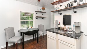 A kitchen with a dining table, chairs, a coffee maker, and shelves with kitchen items. - Riverfront Hideaway/Kayaks/Pet‑Friendly/Beautiful Views! (Noblesville)