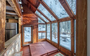 Eine Holzhütte mit großen Fenstern, einer Sitzbank und einem Kühlschrank.