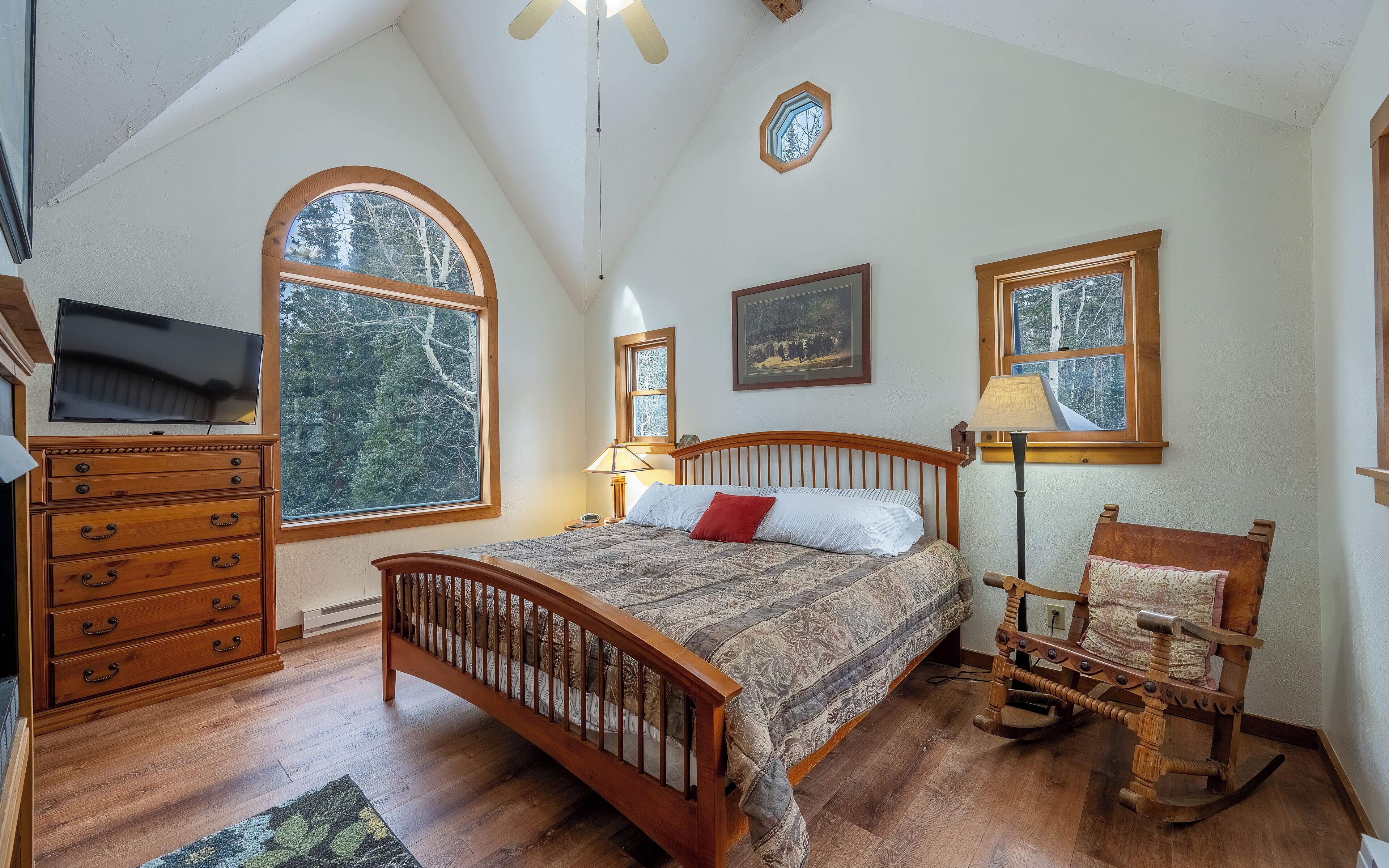 Un dormitorio con una cama grande, cómoda de madera y varios ventanales.