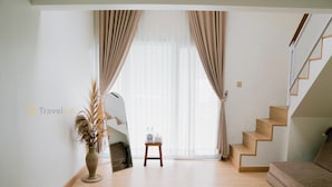 En rummelig opholdsstue med trægulv, en sofa, et lille bord med en vase med tørrede planter, og en trappe op til et højere niveau.