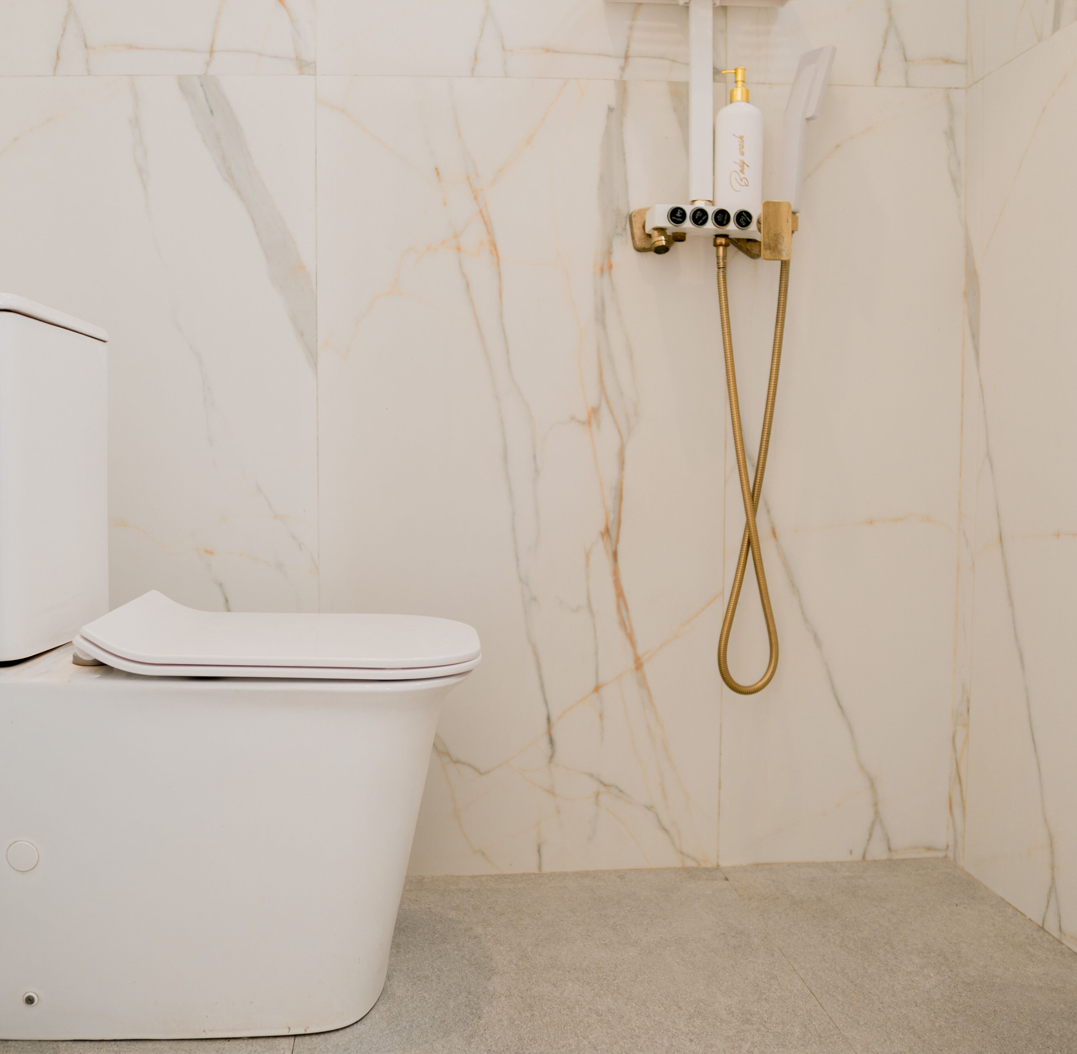 Egy modern fürőszoba, amelyben WC, márványburkolatú falak és arany szín ű zuhanycsaptelep található.