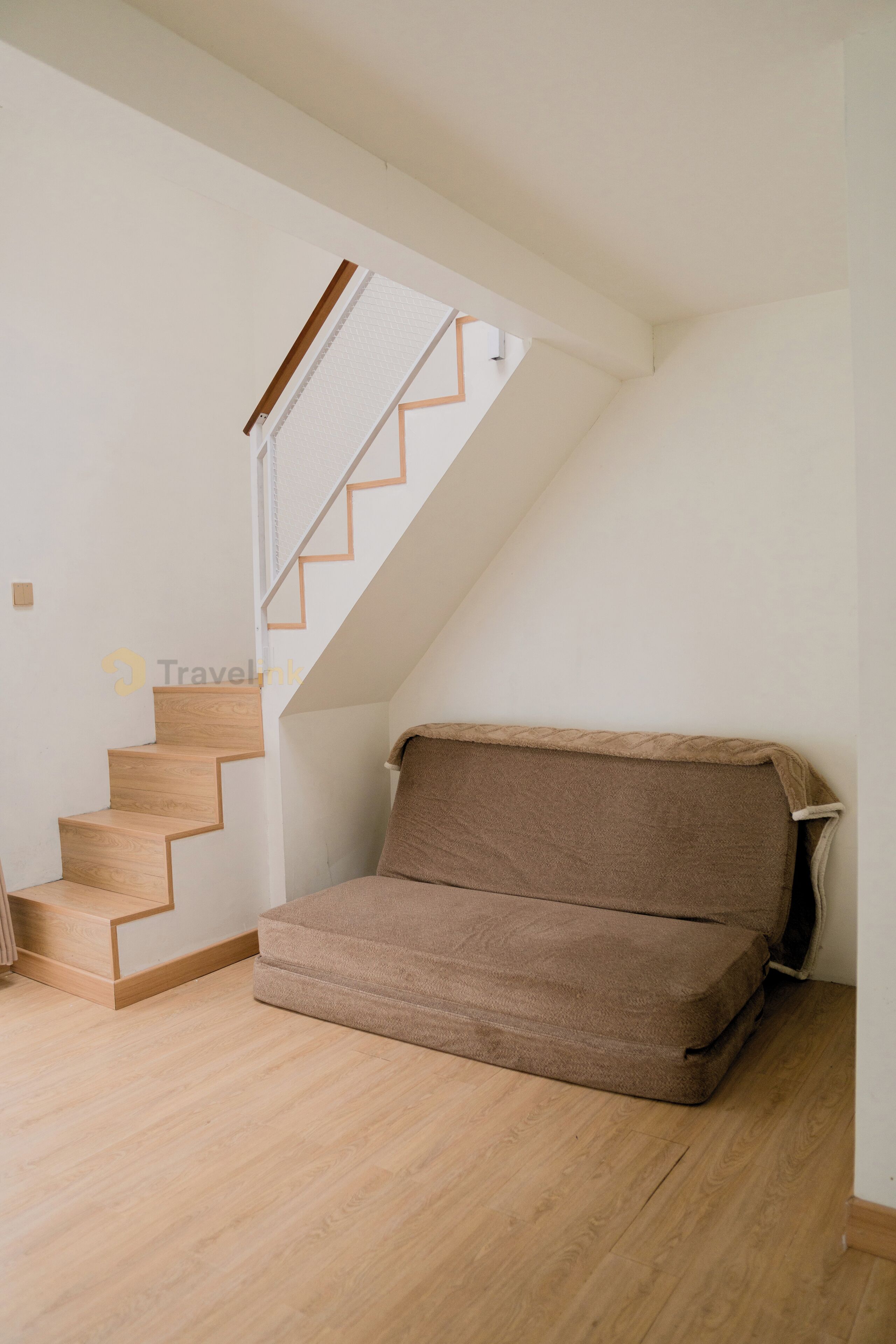 Una habitación con una escalera de madera, un sofá marrón y una pared blanca.