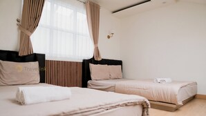 Et hotelværelse med to senge, et vindue med gardiner, en vægmonteret lampe og trægulv.
