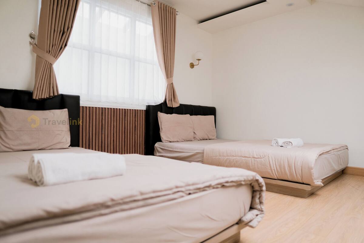 A hotel room with two beds, a window with curtains, a wall-mounted light, and a wooden floor.