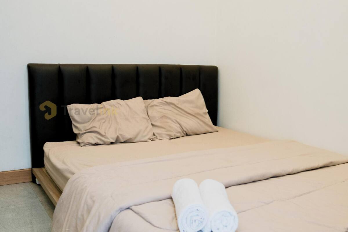 A neatly made bed with a black headboard, beige bedding, and two rolled towels on the foot of the bed.