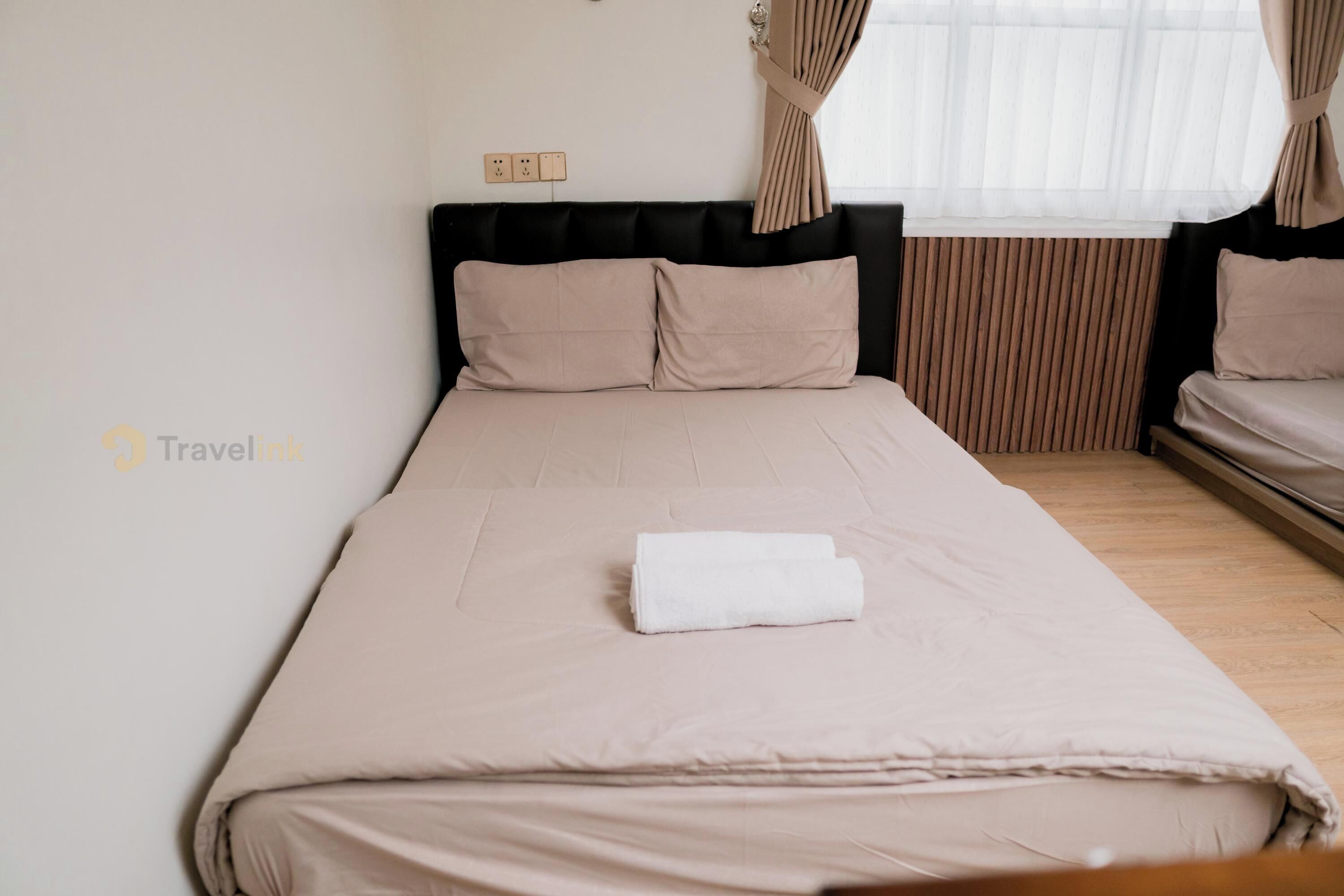 A neatly made bed with a white towel, a black headboard, and a window with curtains.