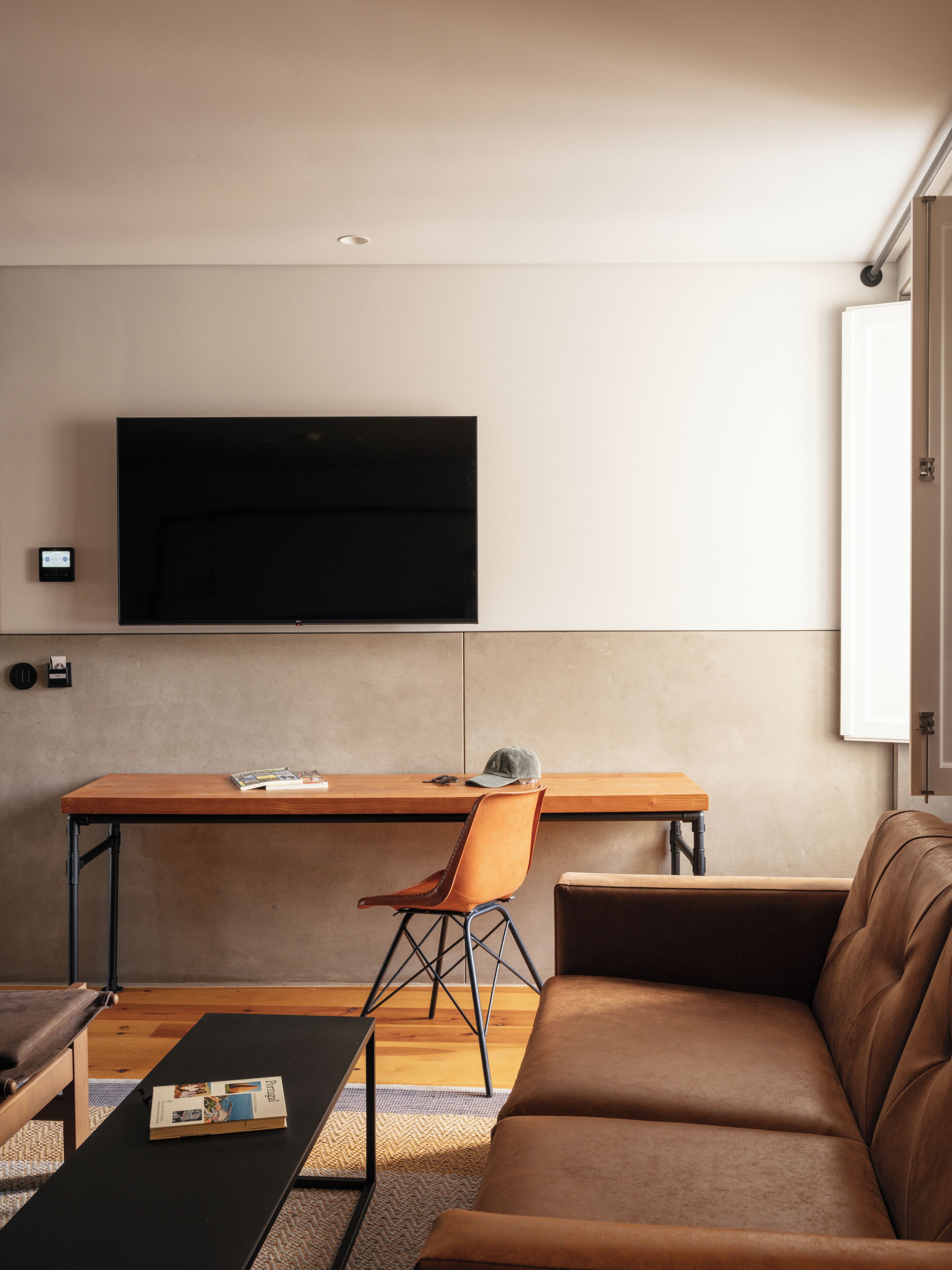 A modern living room with a sofa, a coffee table, a desk with a chair, and a flat-screen TV mounted on the wall.