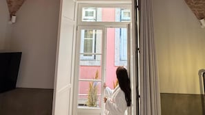 Ein Zimmer mit Backstein-Decke, einem Bett, einem Stuhl und einem Fenster mit Blick auf Gebäude.