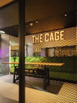 A restaurant interior with a neon sign reading "THE CAGE" and a seating area with tables and chairs.