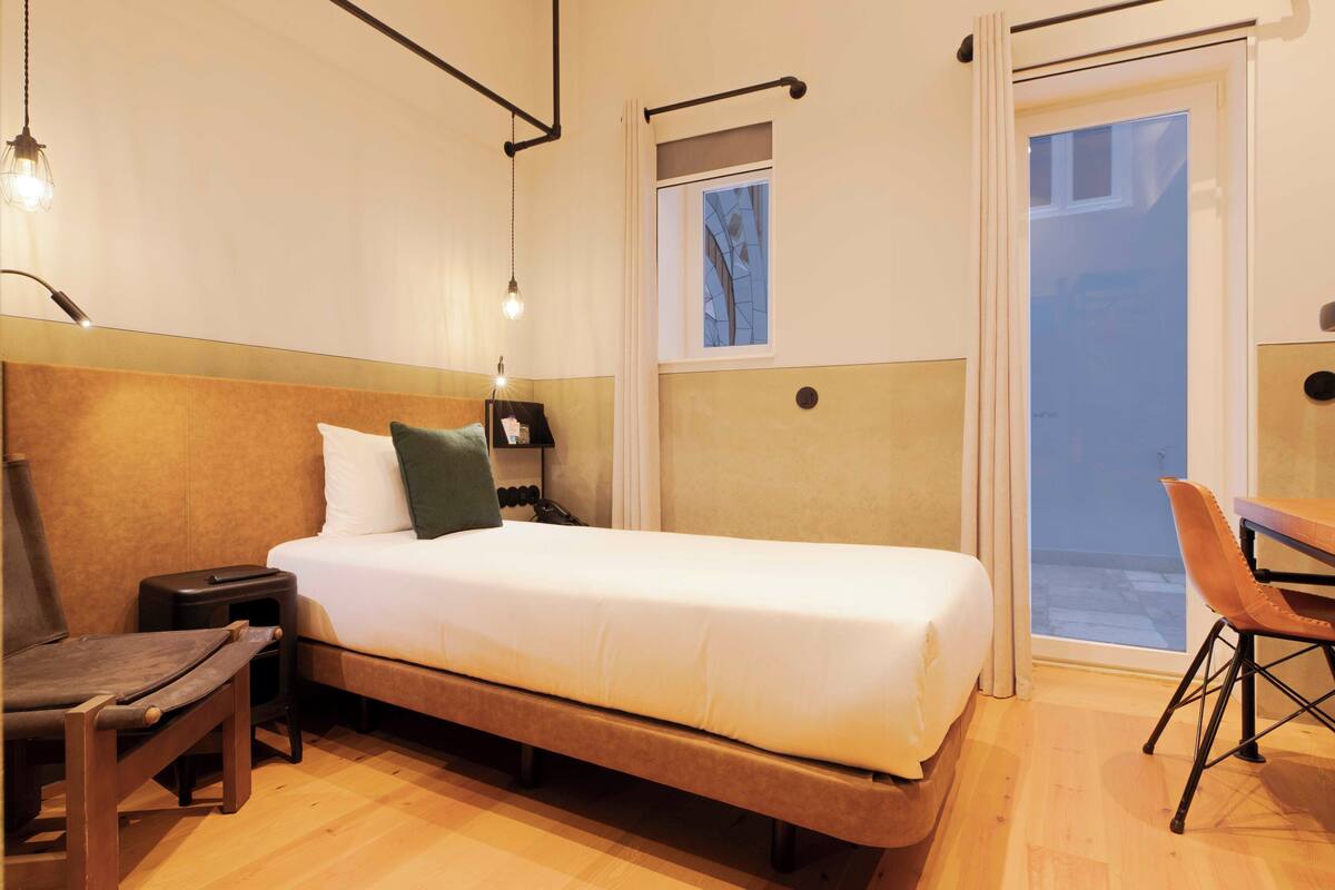 Un dormitorio con cama, mesita de noche, lámpara, silla y ventana con vistas.