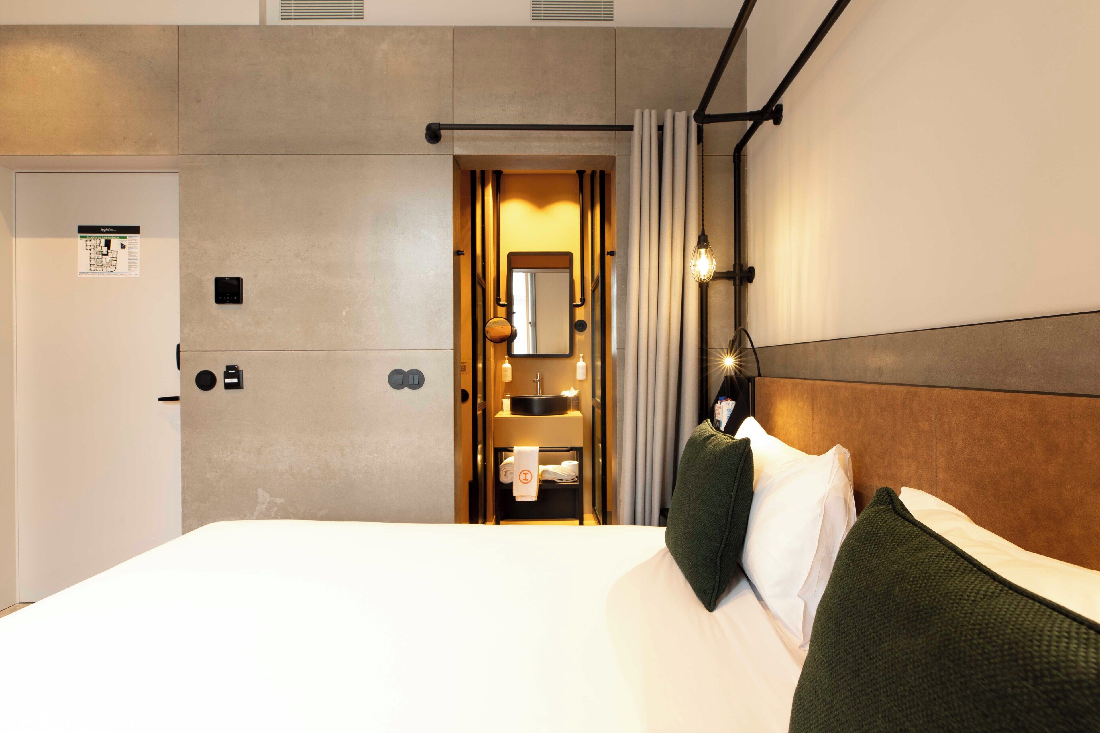 A hotel room with a bed, a bathroom with a mirror, and a towel rack.