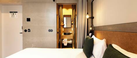 A hotel room with a bed, a bathroom with a mirror, and a towel rack.