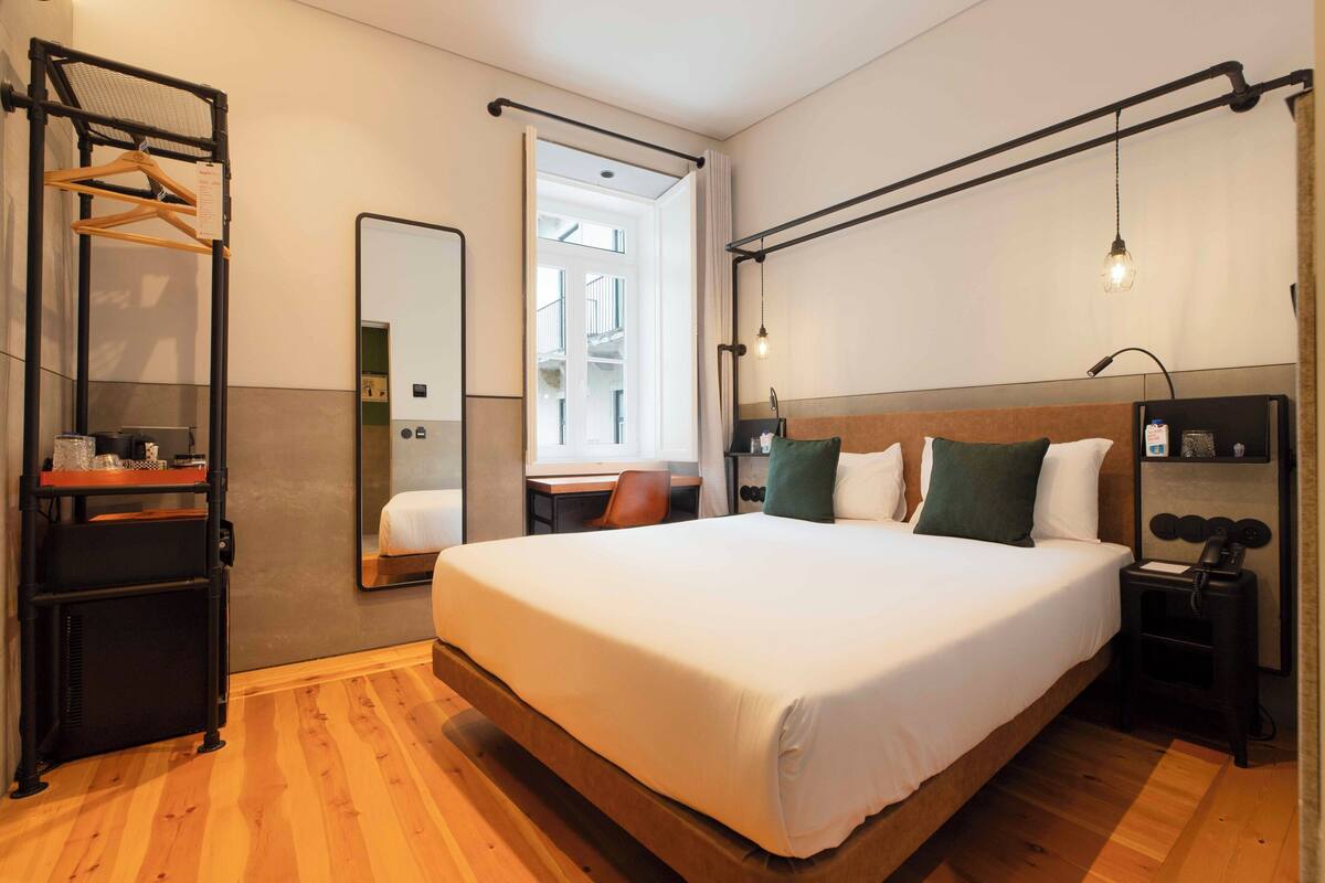 Habitación de hotel con una cama grande, un escritorio, una silla, un espejo, un armario y una lámpara colgante.