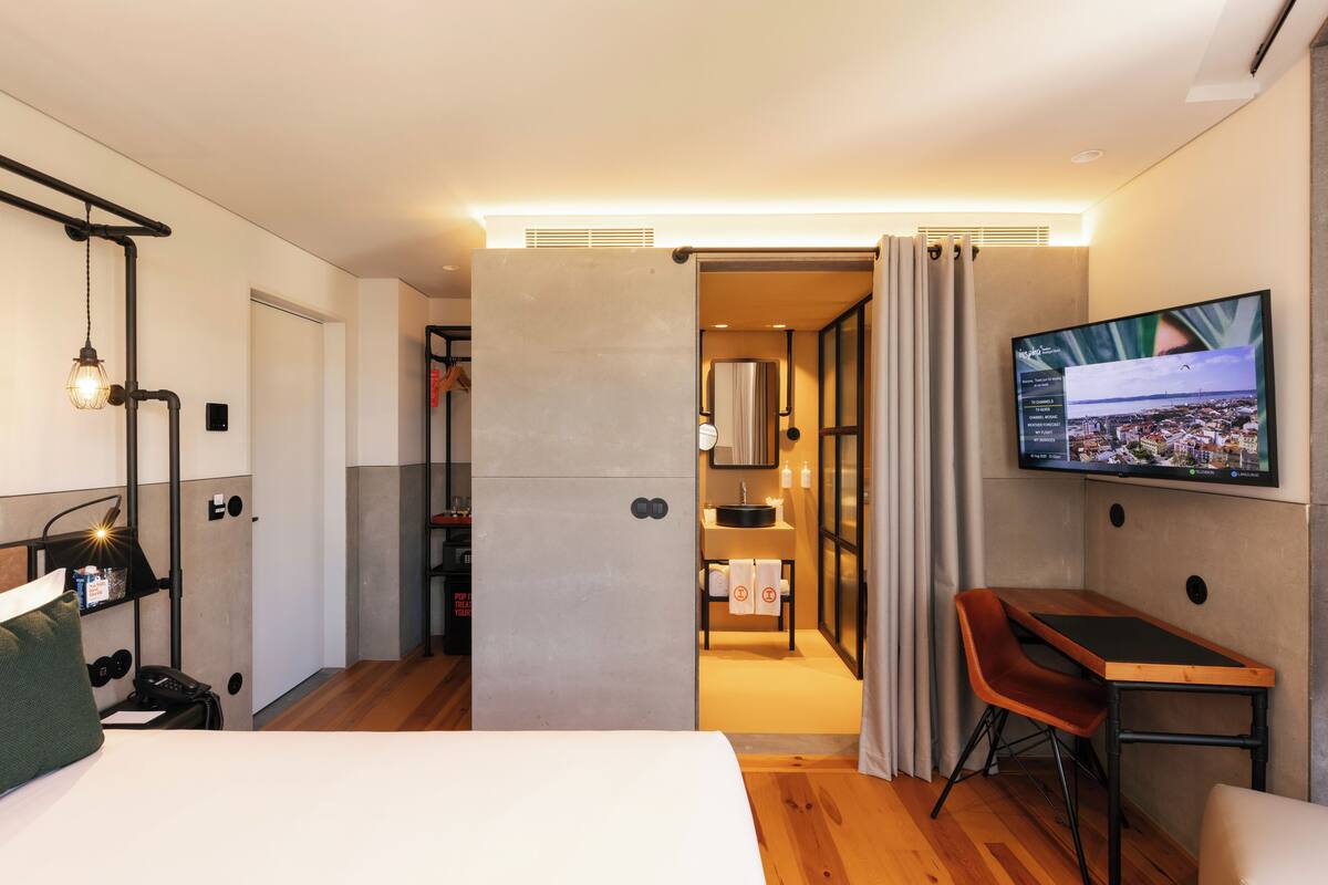 Una habitación de hotel moderna con cama, escritorio, televisor y baño visible a través de una puerta abierta.