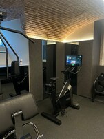 Un gimnasio con equipo de ejercicio, una pantalla en la pared y un techo con textura.