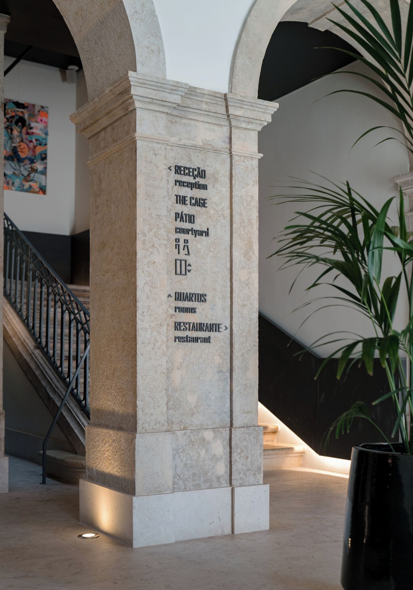 Un espace d’accueil avec un pilier en pierre sur lequel sont affichés des panneaux indiquant la direction à suivre pour se rendre à la réception, à l’enclos, à la cour, aux chambres et au restaurant.