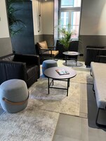 A modern lounge area with leather sofas, a round table with magazines, and a potted plant.