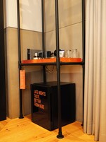 A compact kitchenette with a black refrigerator, a small orange shelf, and a black coffee machine.
