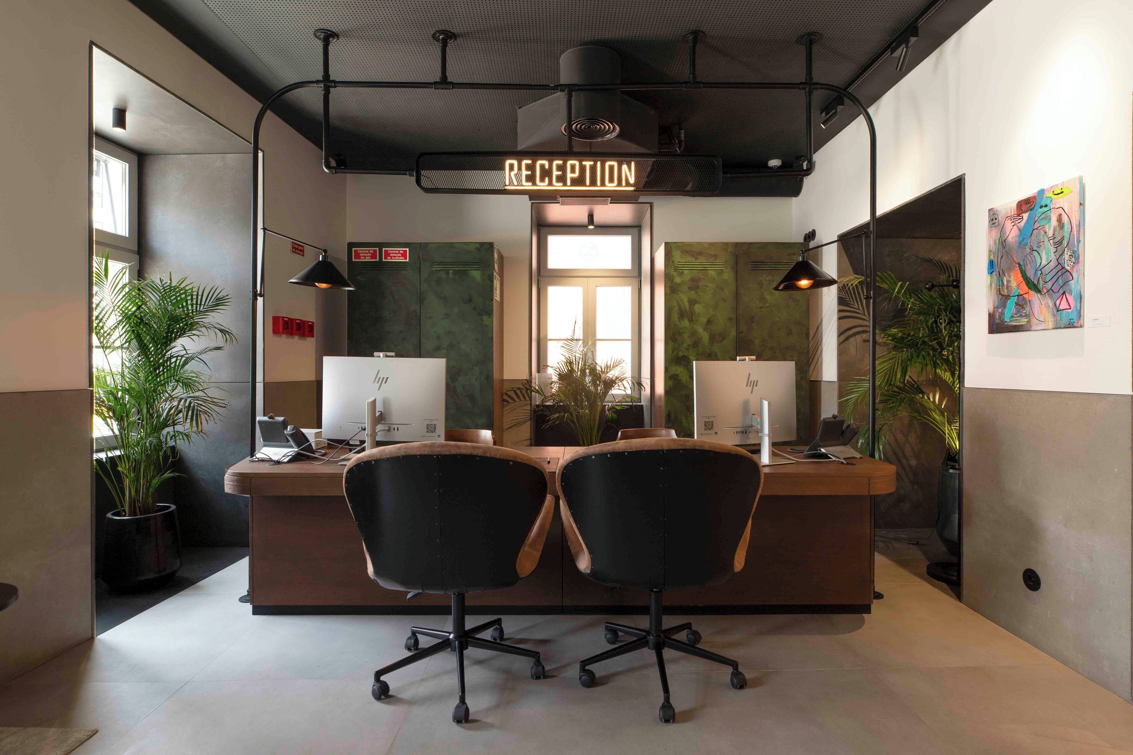 Un mostrador de recepción con un letrero de neón, dos sillas de oficina, una computadora y una planta en maceta.