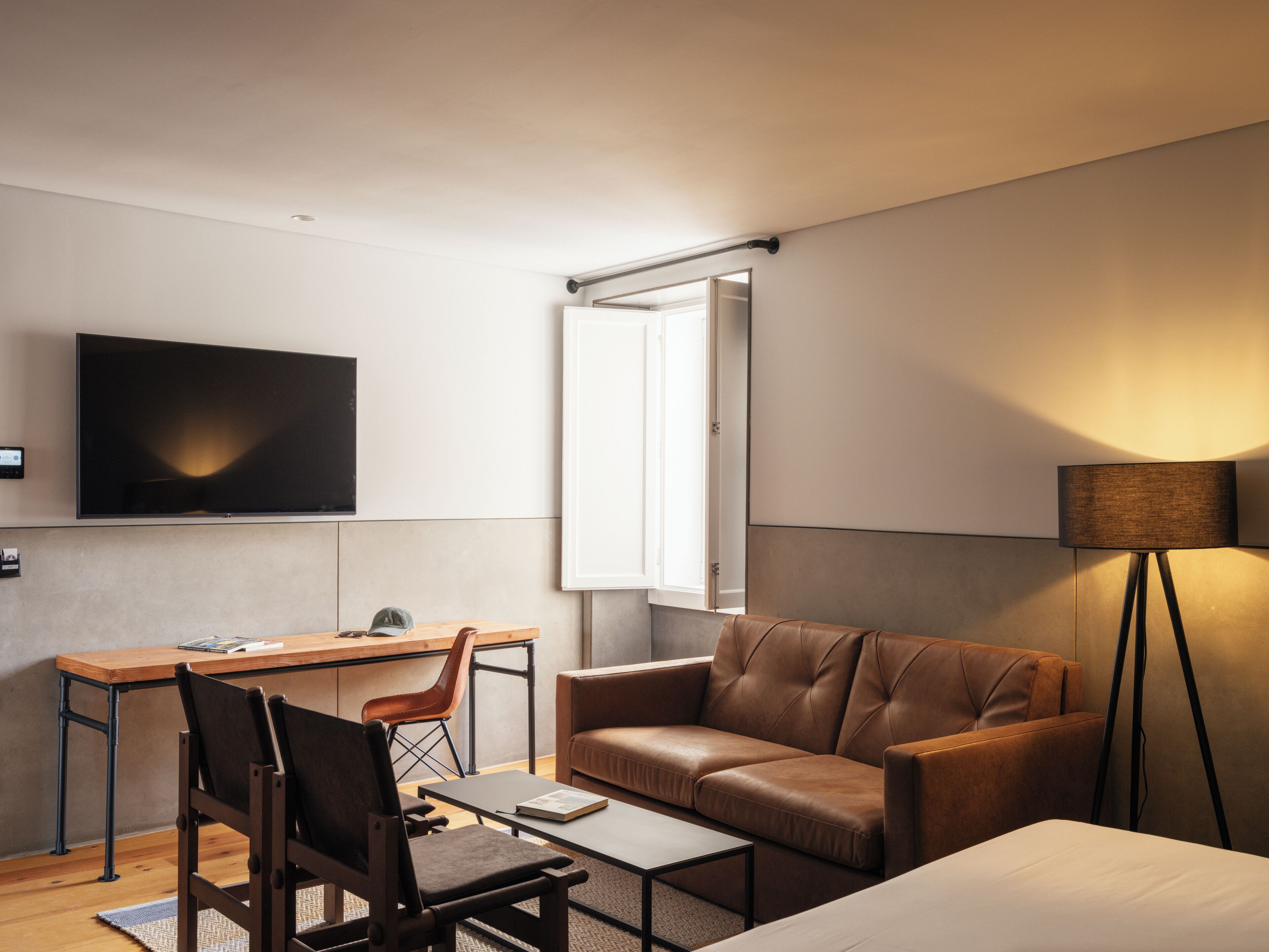 Una camera d'hotel moderna con televisione a schermo piatto, un divano, una scrivania con sedia e una lampada da terra.