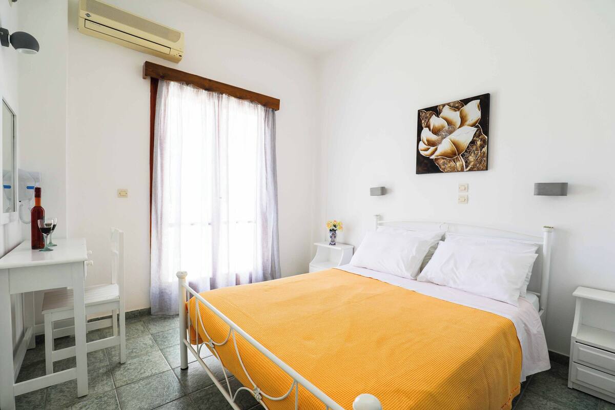 A hotel room with a bed, a bedside table, a chair, a desk, and a window with curtains.