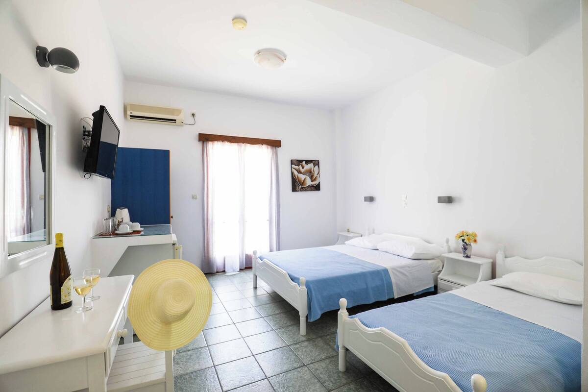 A hotel room with two beds, a desk with a chair, a TV, and a window with curtains.