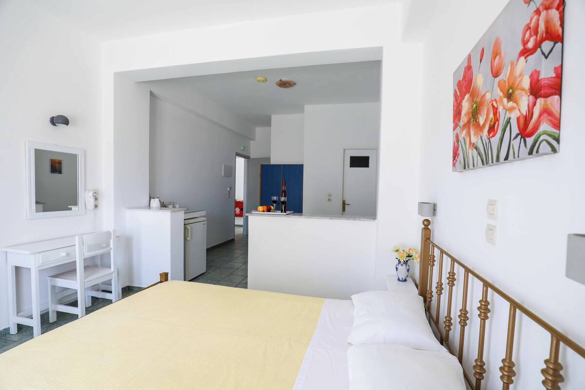 A hotel room with a bed, a desk, a chair, a bathroom, and a kitchen area.