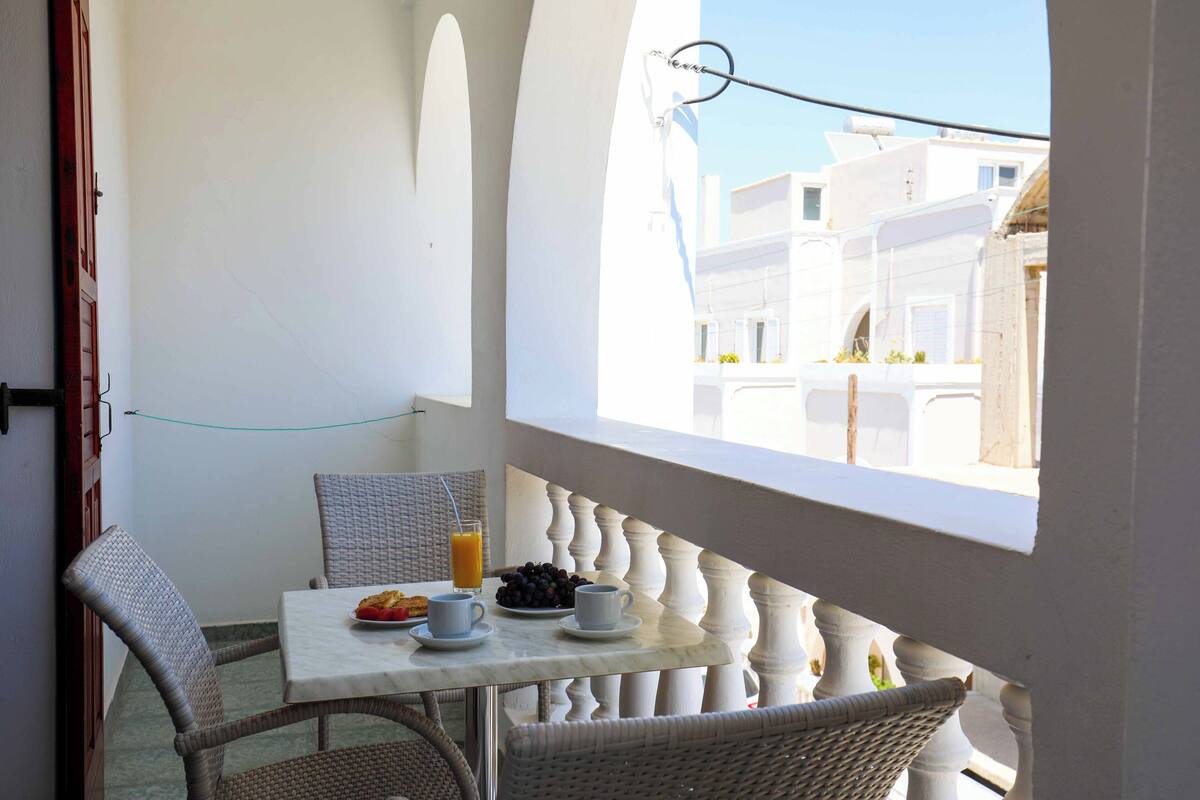 A balcony with a table set for breakfast, wicker chairs, and a view of white buildings.