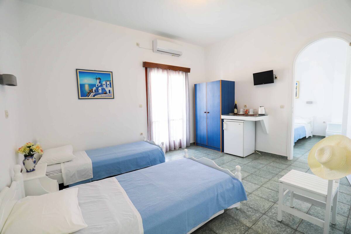A hotel room with two beds, a desk, a television, and a bathroom visible through an archway.