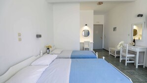 A hotel room with two beds, a desk, a chair, a mirror, and a small table with a vase of flowers. - Finikas Santorini (Kamari)