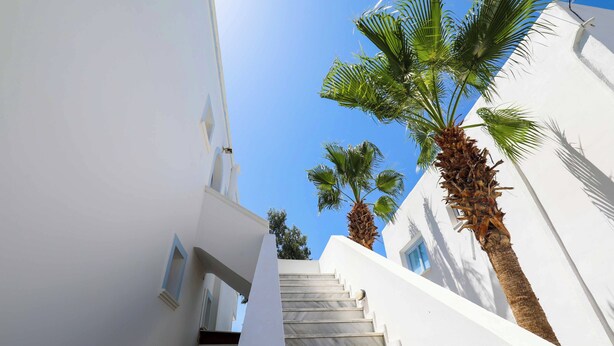 A white building with a staircase leading up to a balcony. - Finikas Santorini (Kamari)
