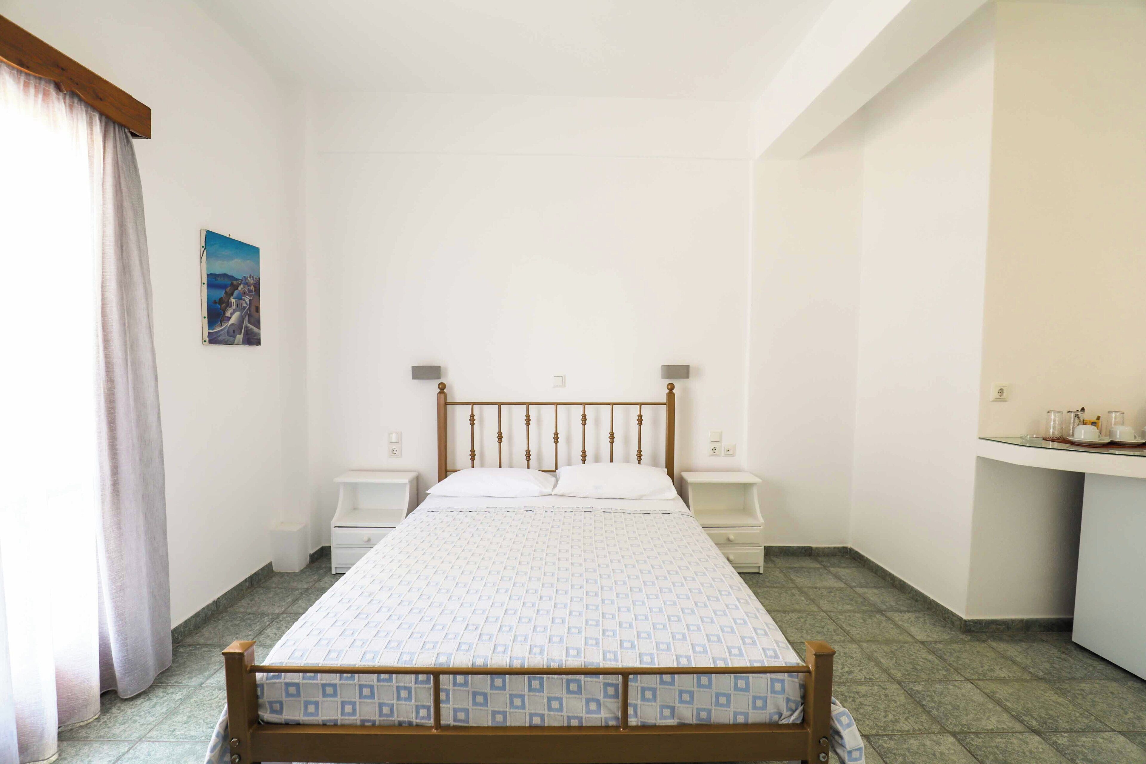 A bedroom with a wooden bed, two bedside tables, a nightstand, a small desk, and a window with curtains.