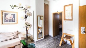 Una camera d'hotel moderna con pavimento in legno, un divano, un tavolino, uno specchio e una porta che dà su un'altra stanza.
