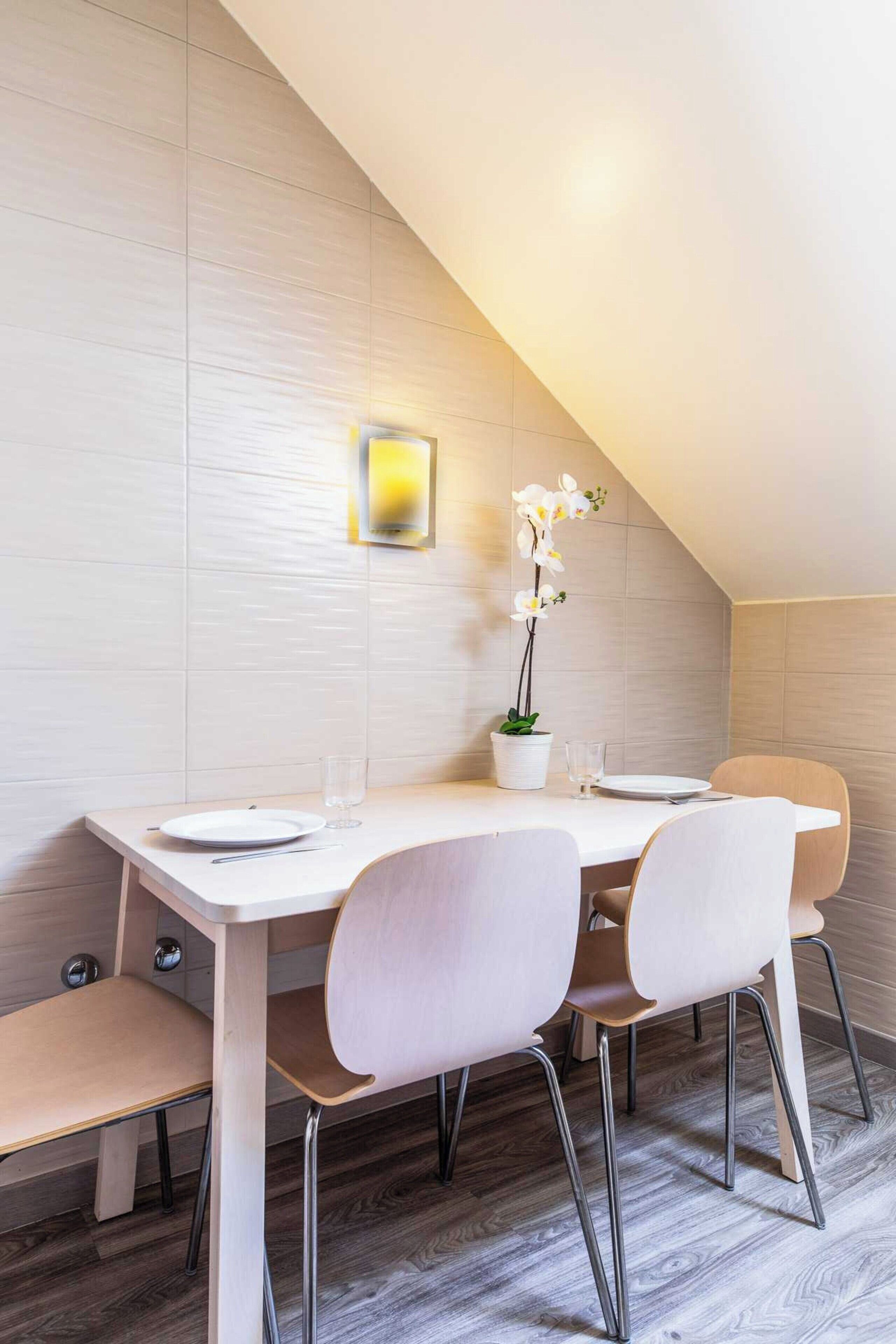 A dining area with a white table, four chairs, and a potted orchid.