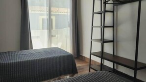 Ein Zimmer mit einem Bett, einem kleinen Tisch, einem Kleiderschrank und einem Fenster mit Vorhängen.