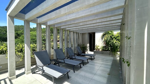 Un espacio de estar techado al aire libre con sillones reclinables y vistas a zonas verdes.