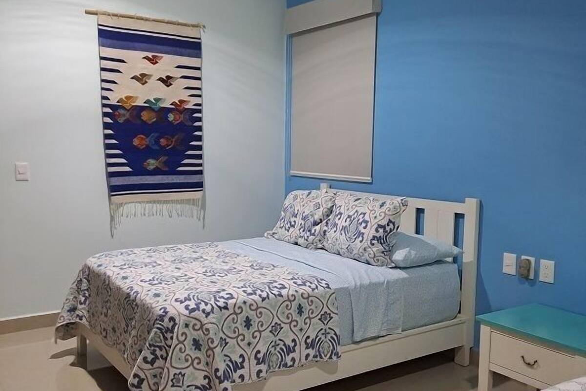 A bedroom with a bed, a bedside table, a wall-mounted air conditioner, and a poster on the wall.