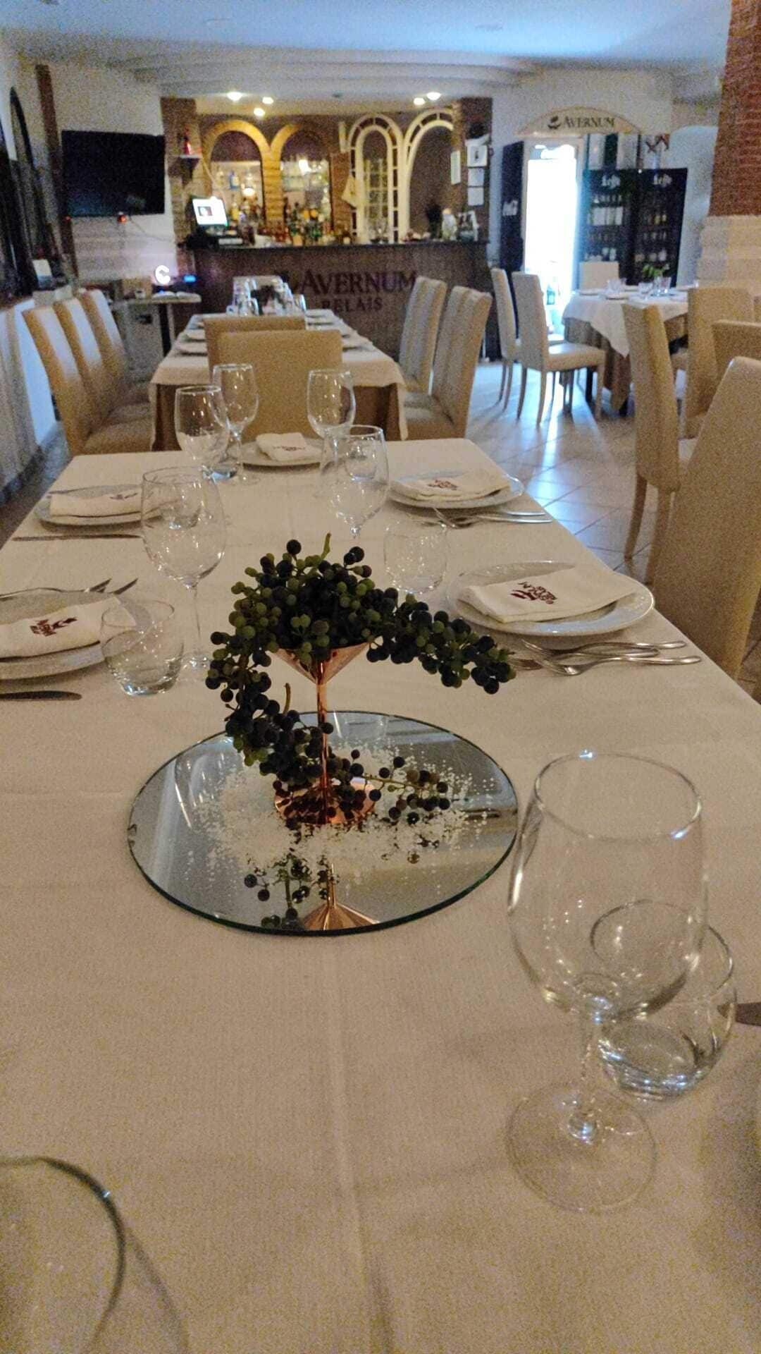 A dining table set for a meal with a centerpiece of grapes and a glass bowl.
