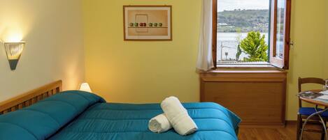 Un dormitorio con cama, ventana con vistas, una silla y una lámpara de pared.